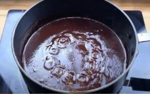 Rich chocolate sauce simmering in a pot on a stovetop, perfect for desserts or toppings.